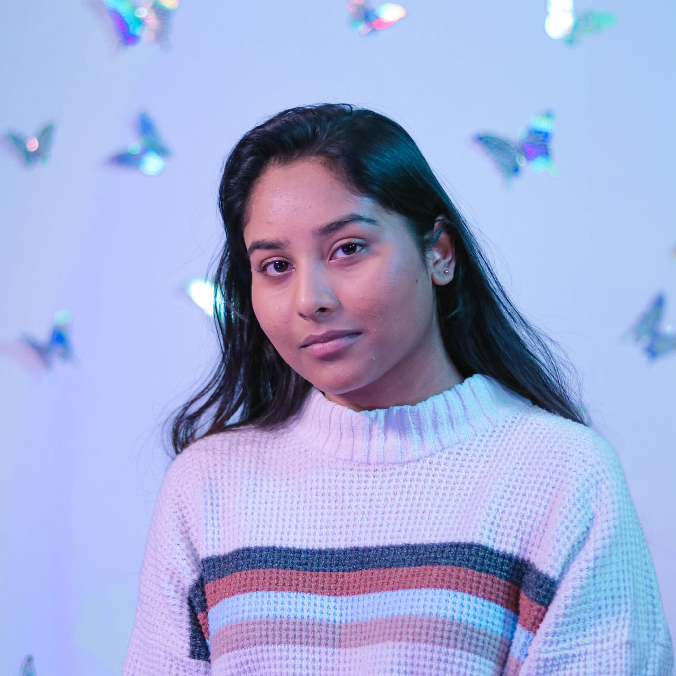 Koshala looks thoughtfully ahead while silver butterflies fill the background.