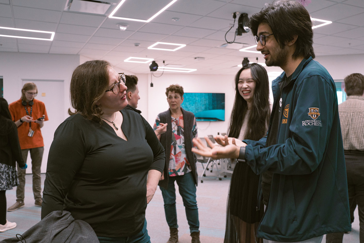 Waleed talks to Kristana Textor while other students, faculty, and staff talk in the background.