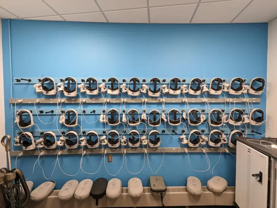 Headset wall with three rows for hanging headsets and controllers and two rows with long power strips for charging.