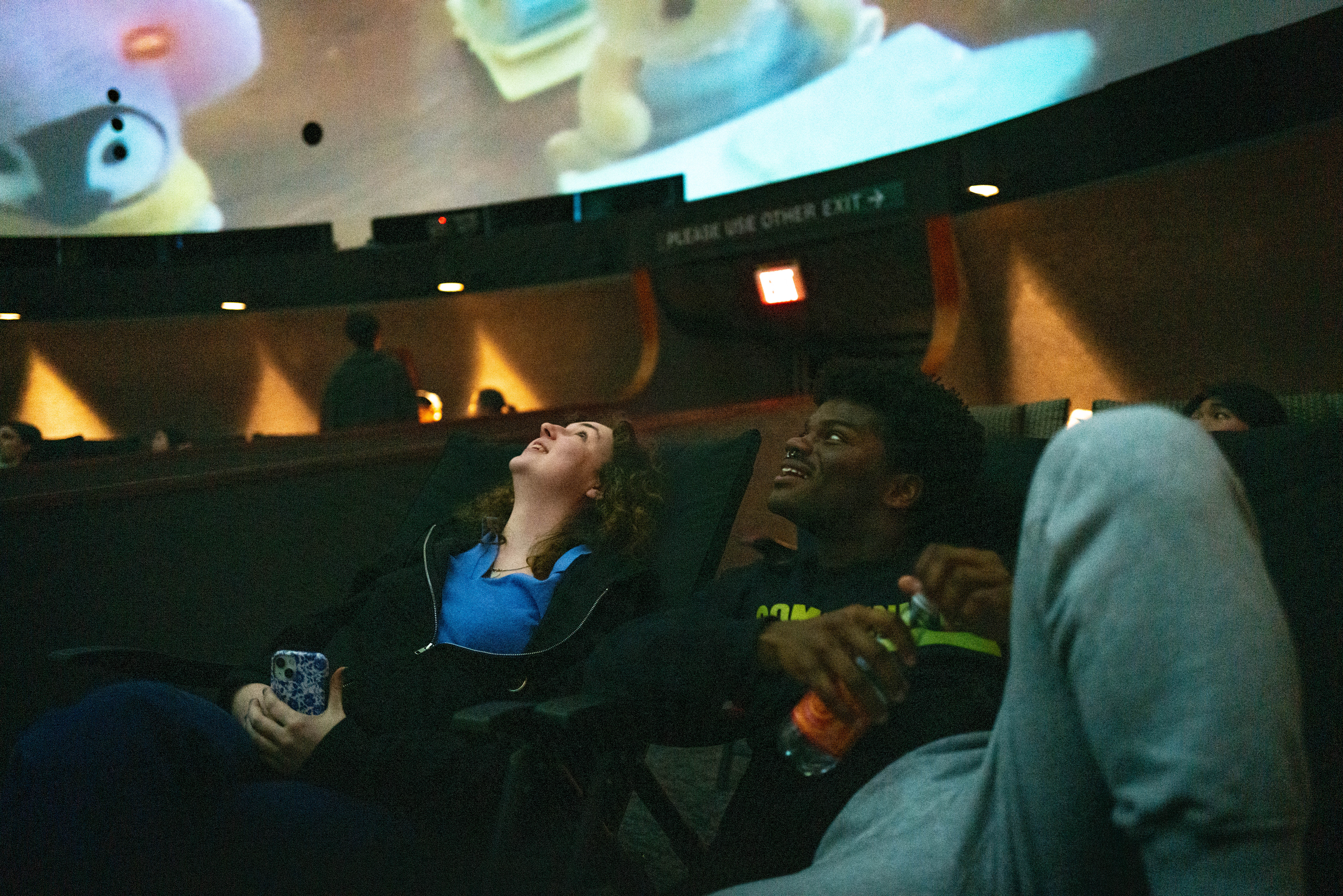 Two students smiling and looking up at immersive film screen.