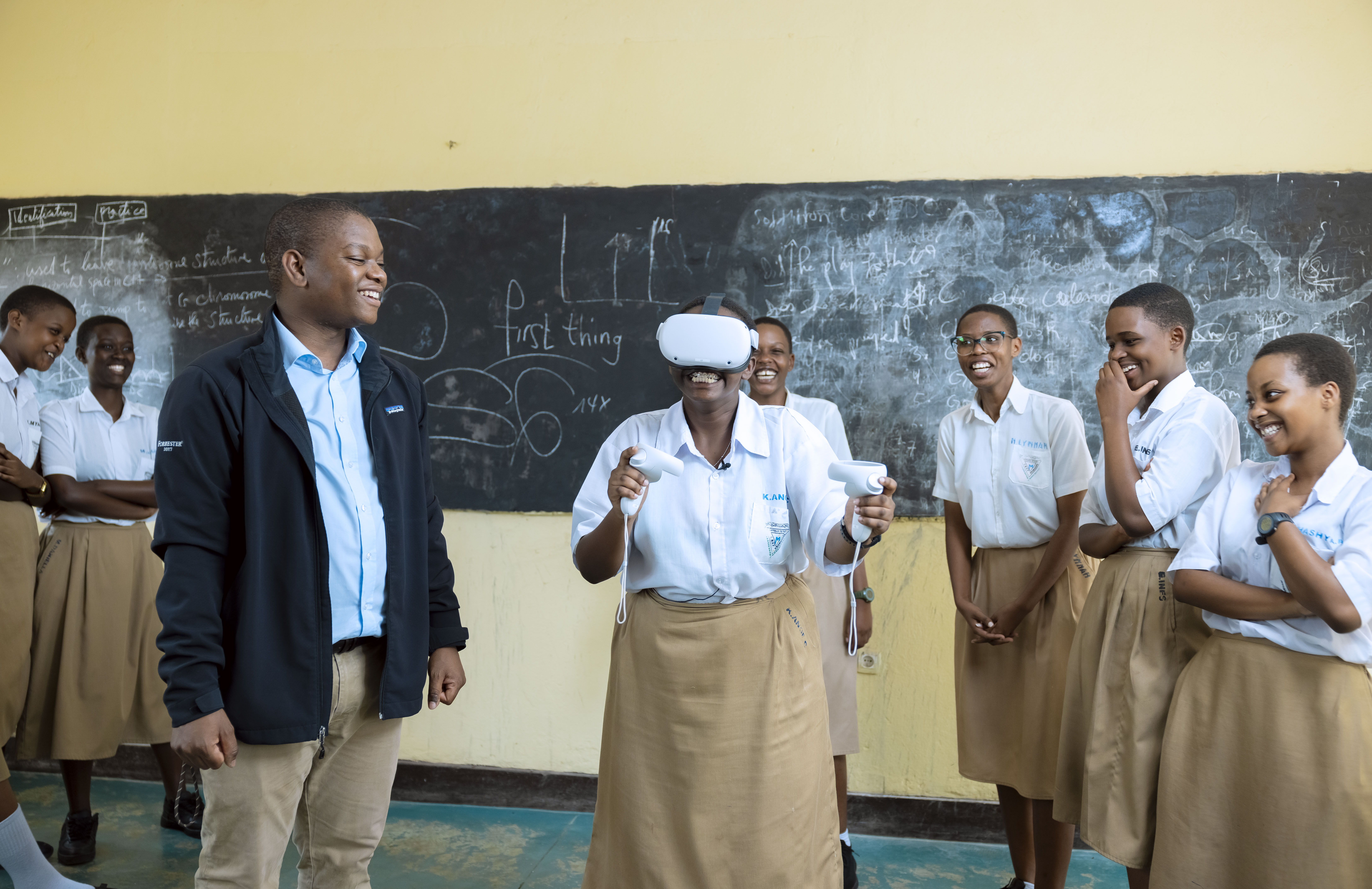 Former Studio X student, Tamuda, gifting and testing VR headset with smiling students at Rwanda's Marie Reine de la Paix school.